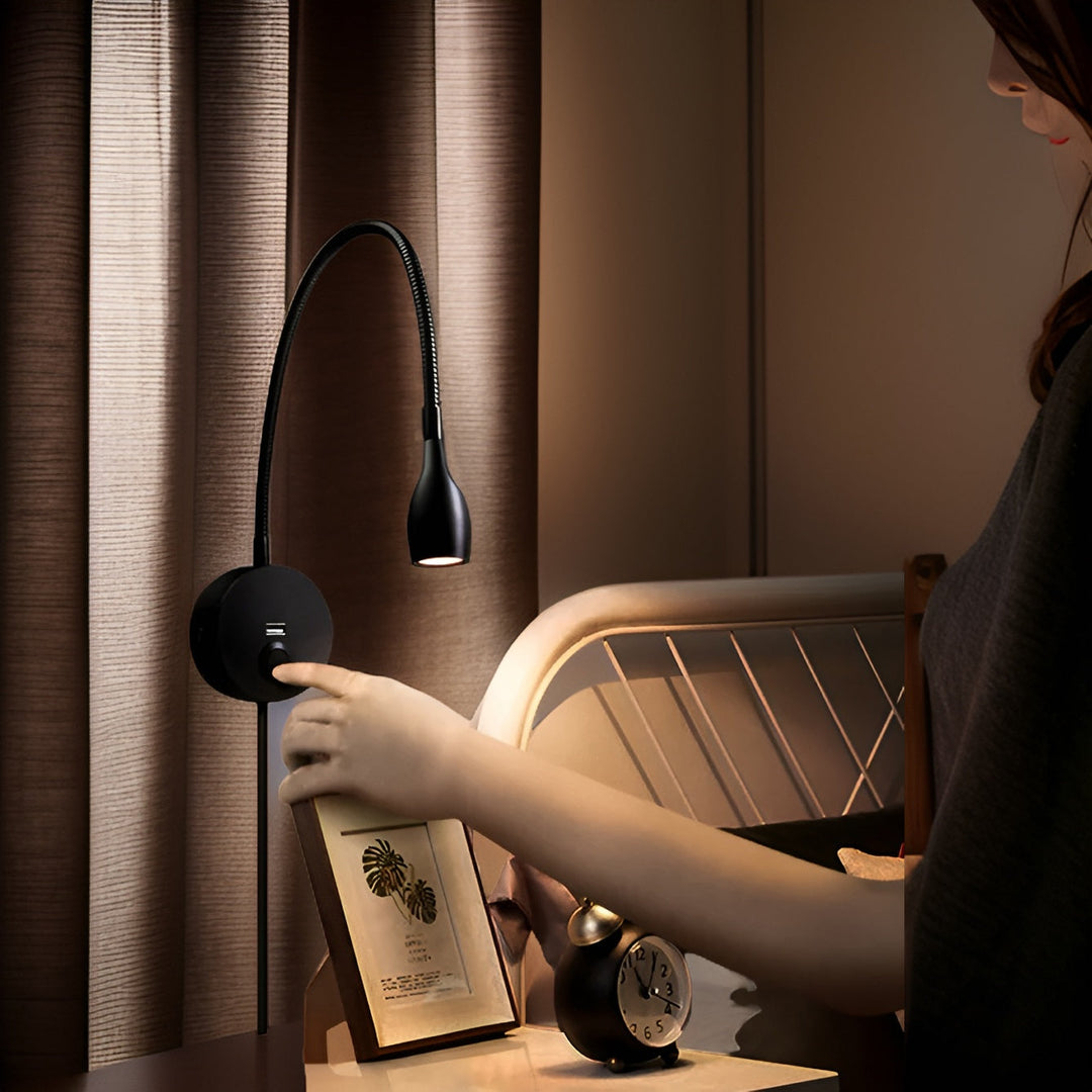 Black adjustable gooseneck wall reading lamp mounted beside a bed with touch control