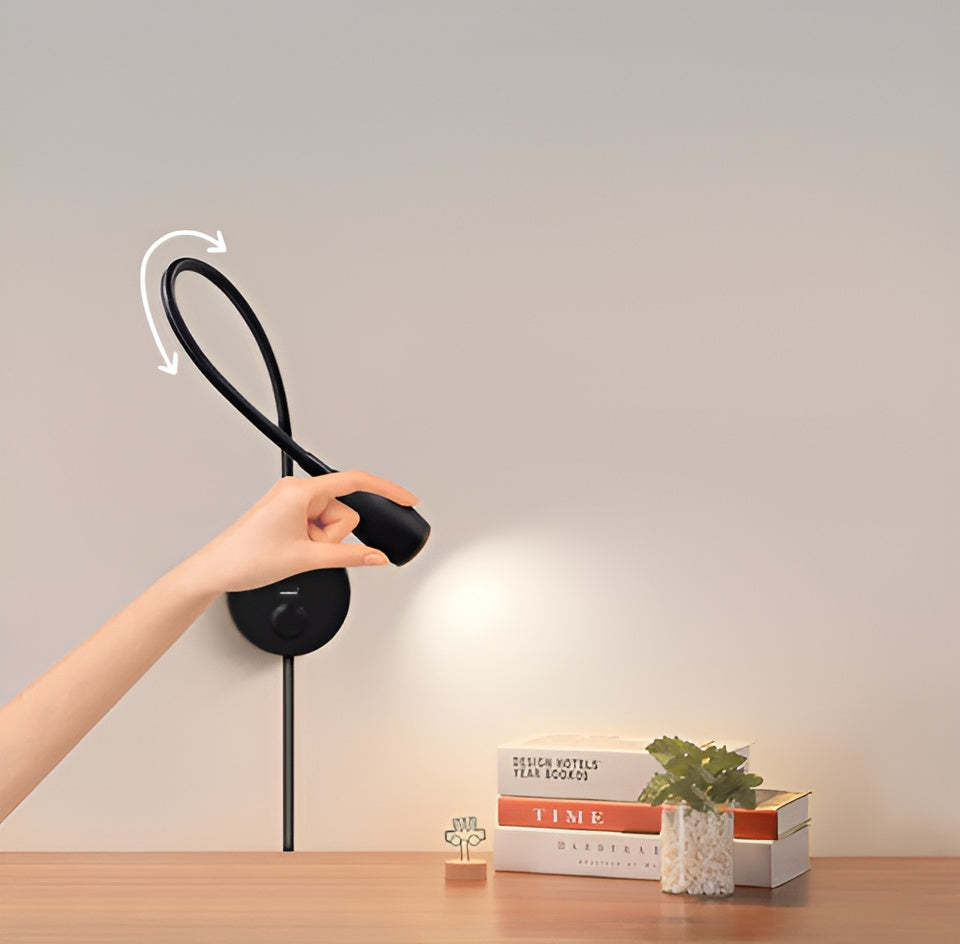Hand bending the flexible arm of the black LED wall lamp over a wooden table