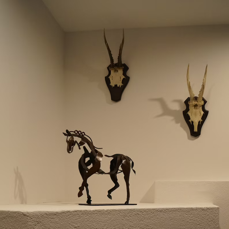 Ferro metal horse sculpture displayed on a white shelf next to wall mounted decor