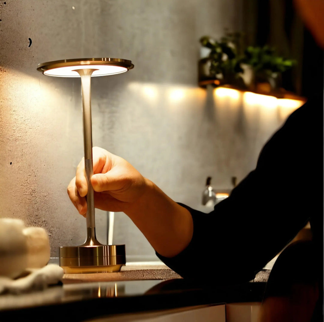 Person operating a gold cordless table lamp on a kitchen counter, showcasing touch activation.
