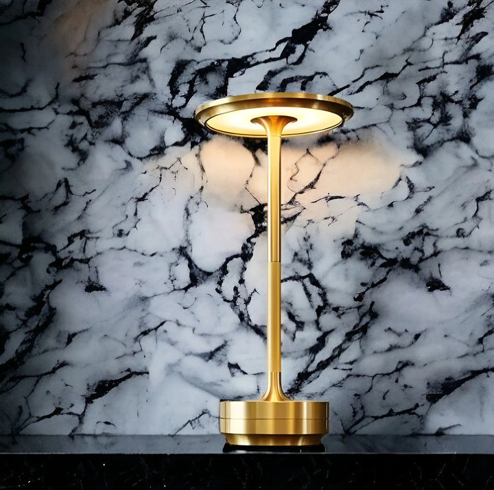 Elegant gold rechargeable touch table lamp glowing against a patterned marble background.