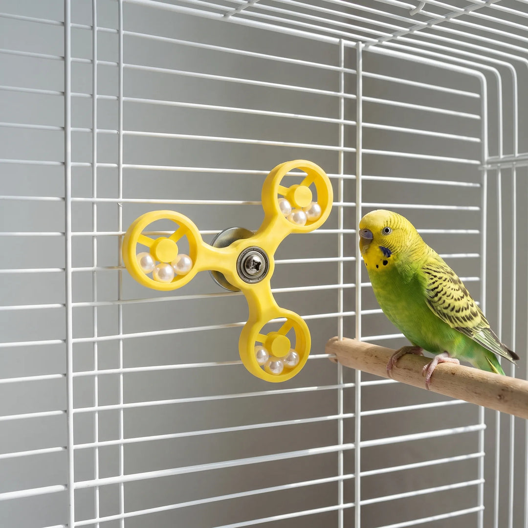 Budgerigar perched near the yellow rotating bird toy in a cage