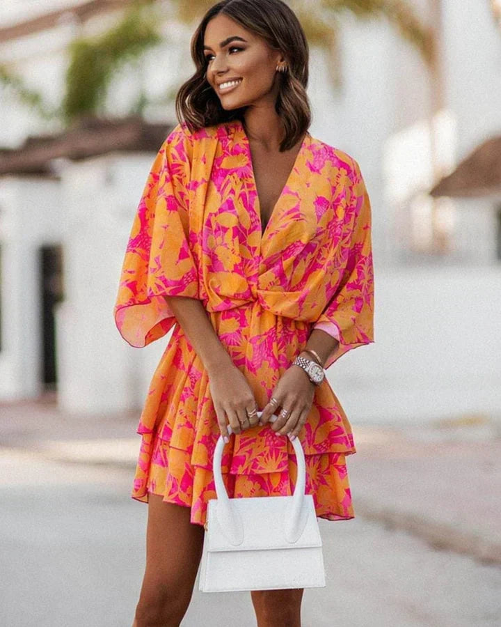 Woman wearing vibrant orange and pink patterned summer dress holding white handbag