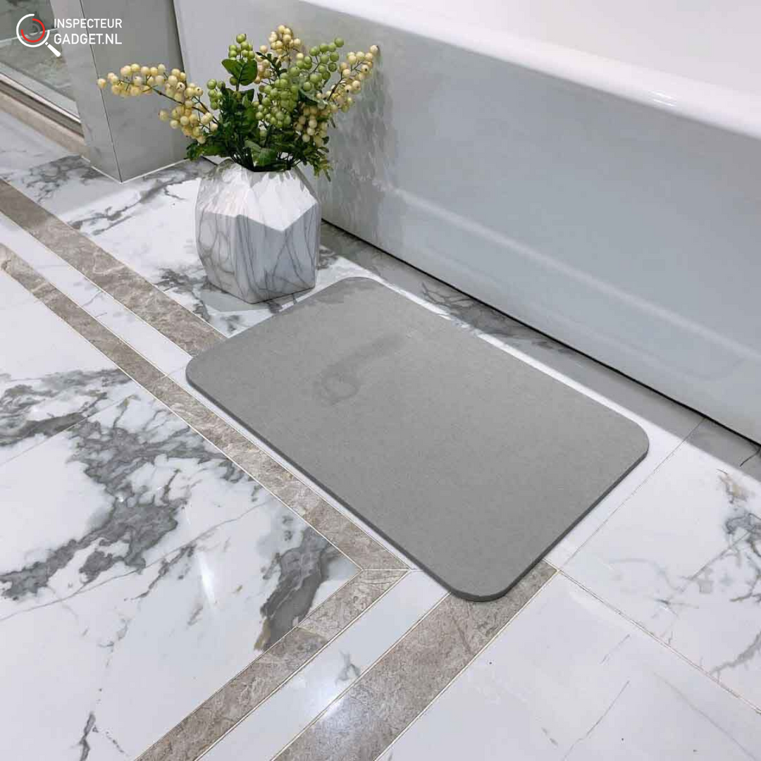 Grey absorbent stone bath mat placed on white marble bathroom floor next to bathtub