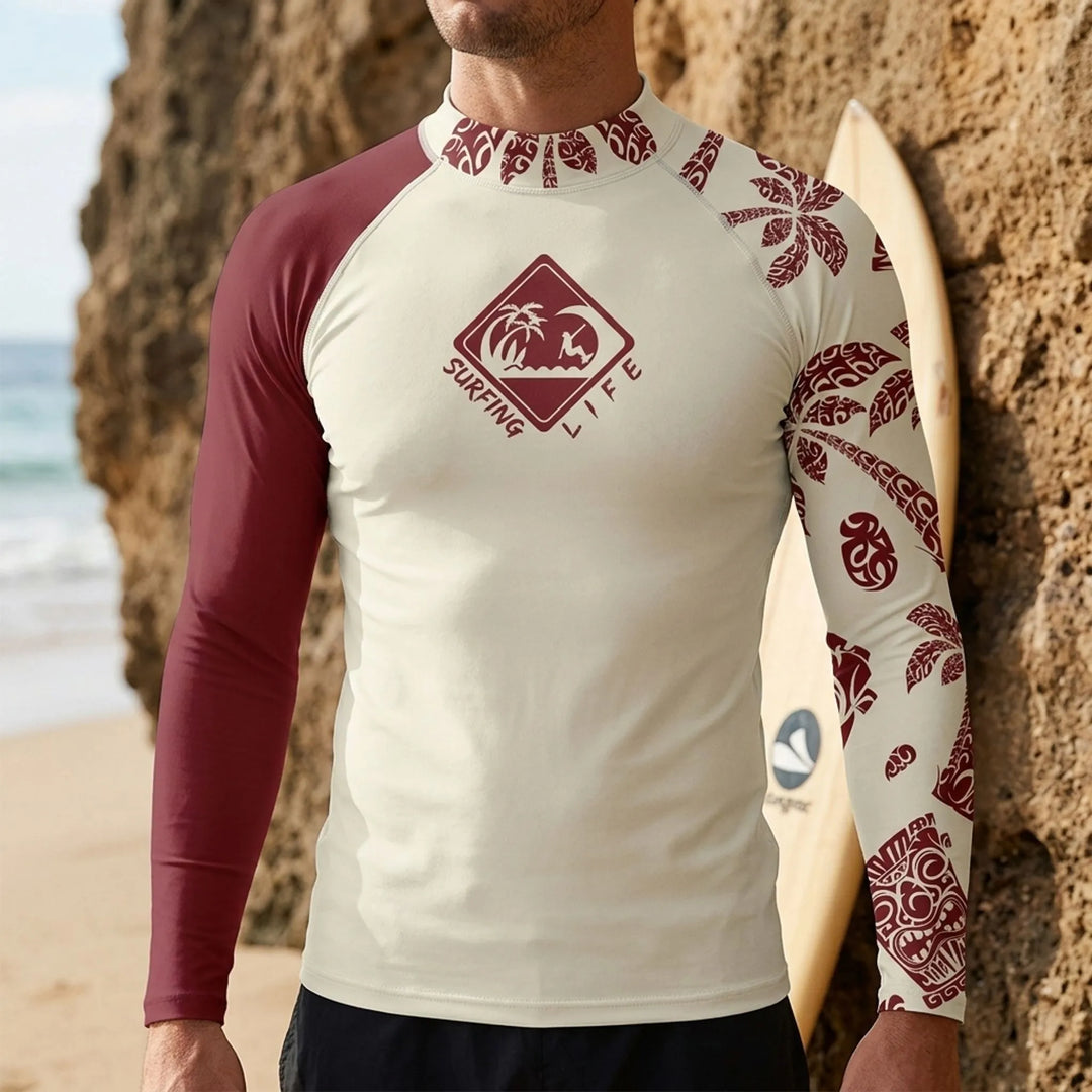 Man wearing a long sleeve rash guard with graphic print outdoors near rocks and a surfboard