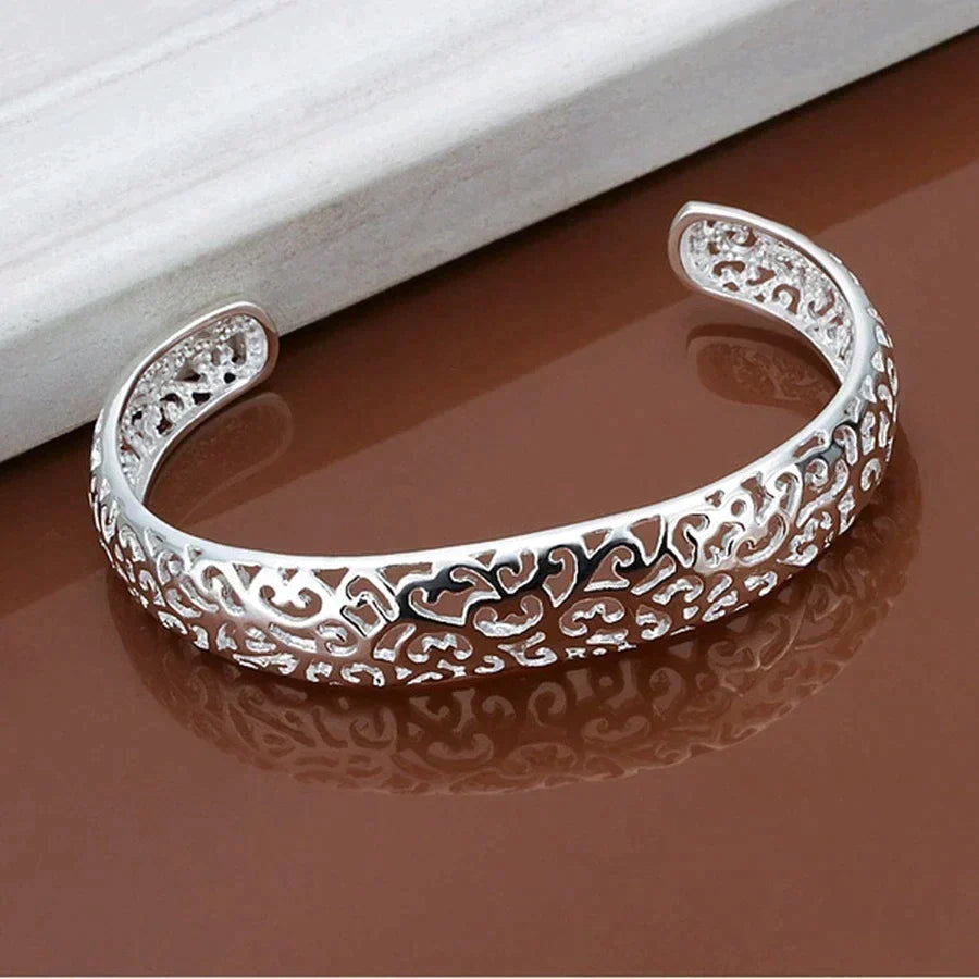 Silver filigree cuff bracelet showcasing openwork pattern on a reflective surface