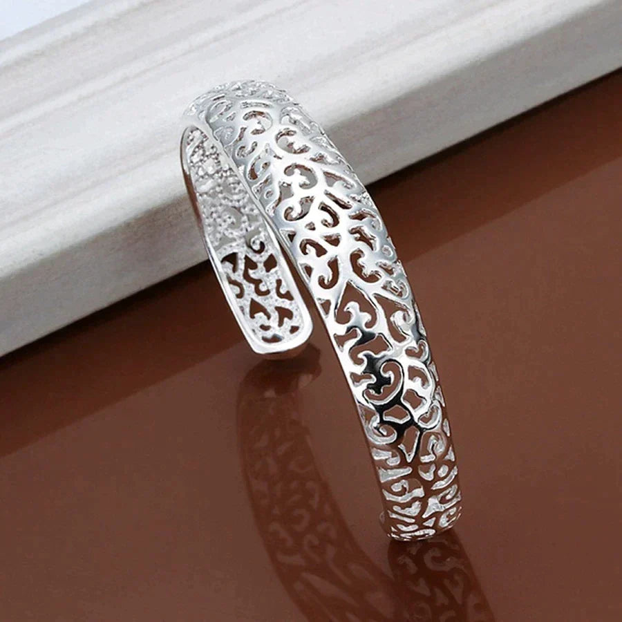 Womens silver filigree cuff bracelet showcasing intricate openwork metal design on a neutral display.