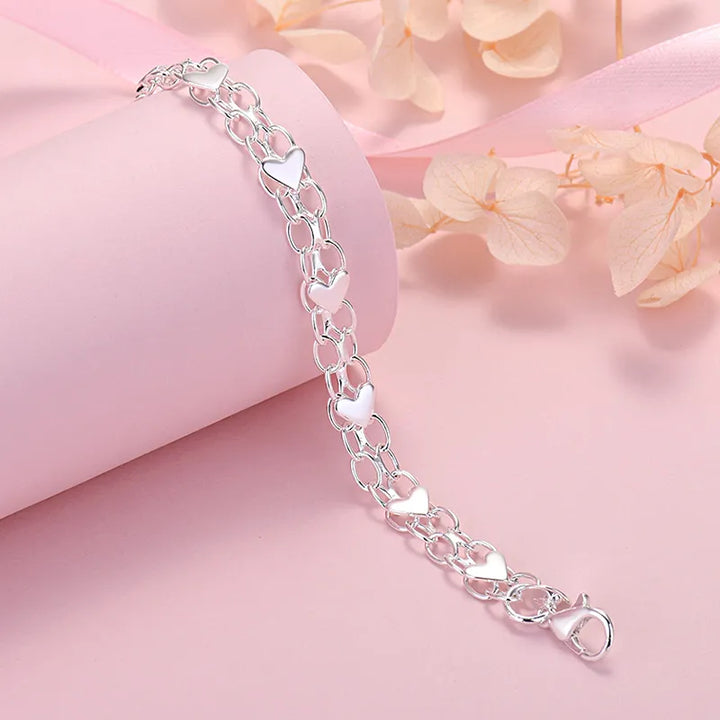 Angled view of silver heart bracelet resting on pink display stand