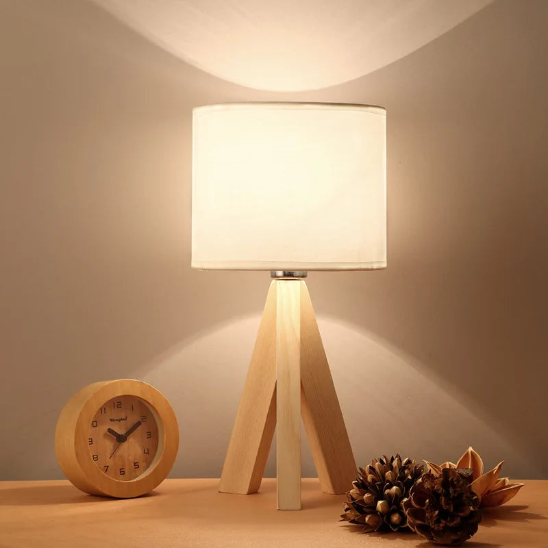 Modern wood opaline tripod table lamp lit on a wooden desk next to decor