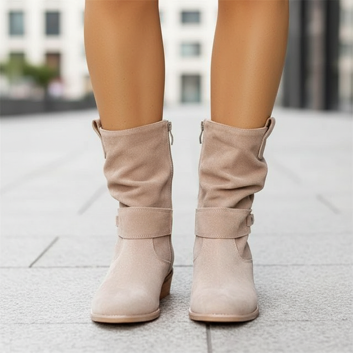 Back view of women wearing beige slouch ankle boots with side zipper and strap detail outdoors on a paved walkway
