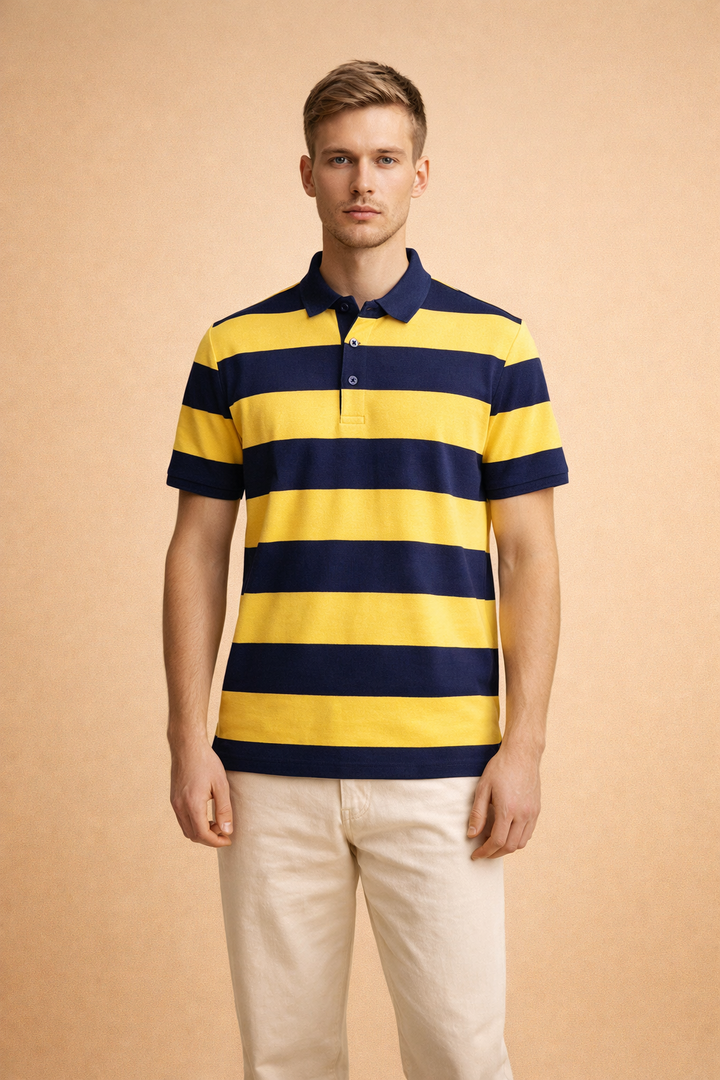 Blonde male model wearing a yellow and navy striped short-sleeve polo shirt and neutral trousers against a warm backdrop.