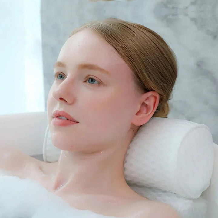 Woman relaxing in a bathtub using a white mesh neck and back support bath pillow