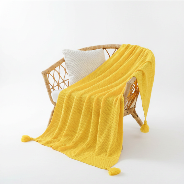 Bright yellow waffle knit throw blanket draped gracefully over a wicker chair
