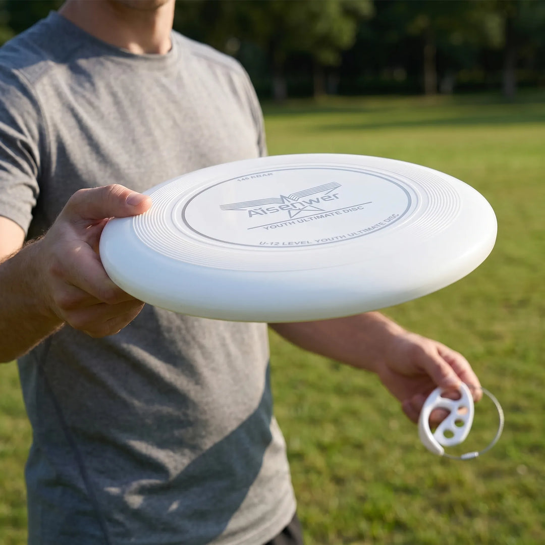 A person holding a white Aeroglide 175g flying disc and handle in a park
