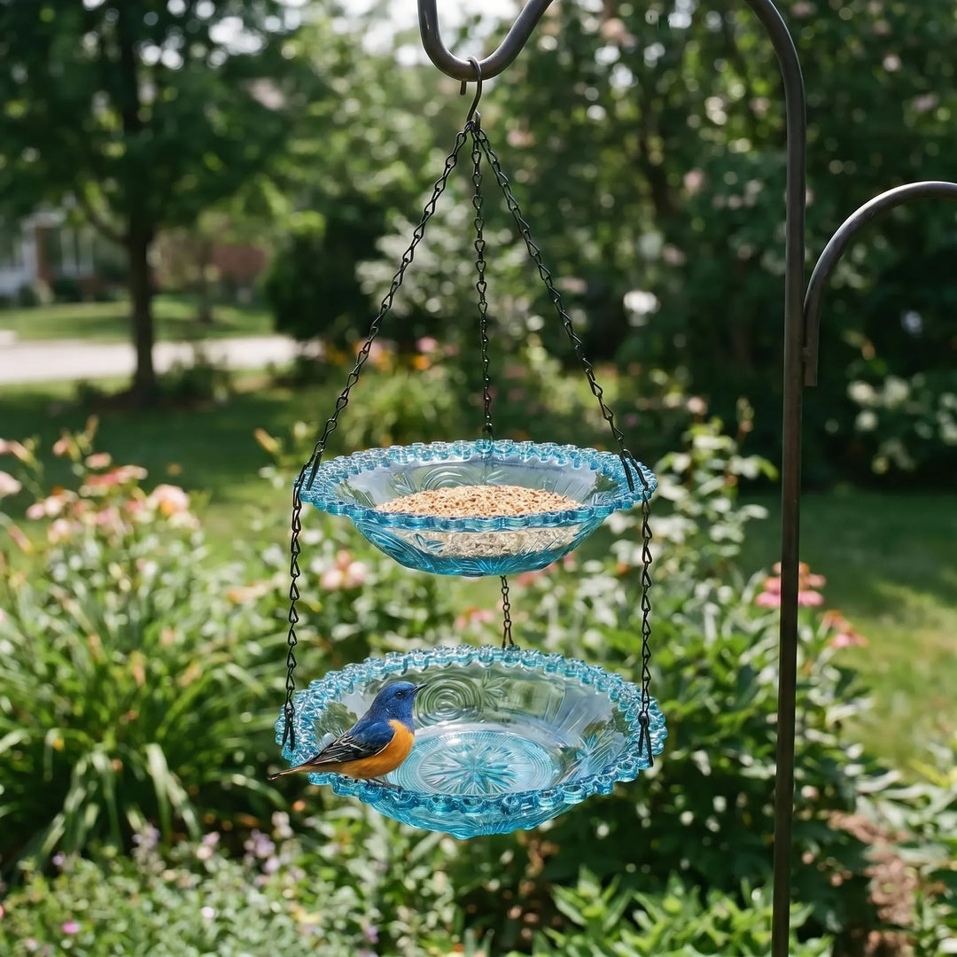 Blue two-layer hanging flower bird feeder suspended from a garden hook with a visiting bird.