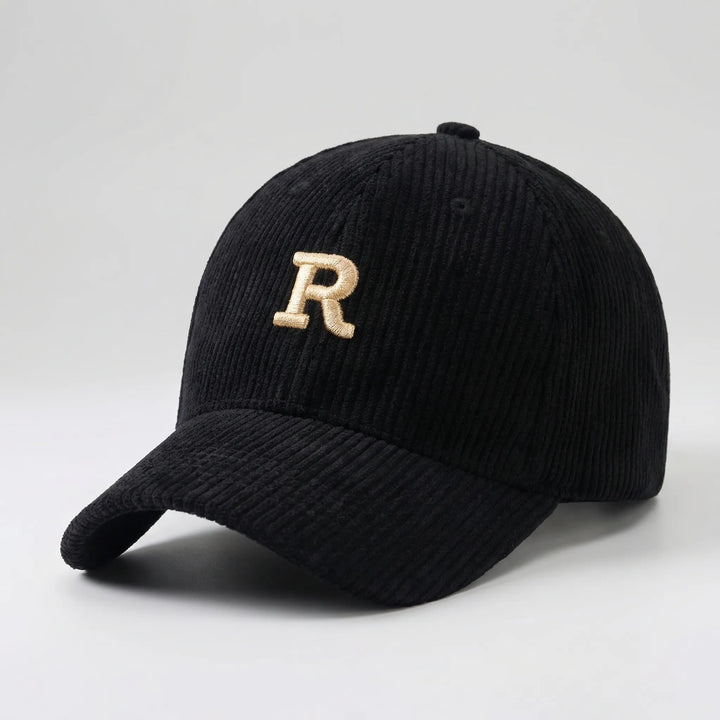 Black structured corduroy baseball cap with gold embroidered letter on white background
