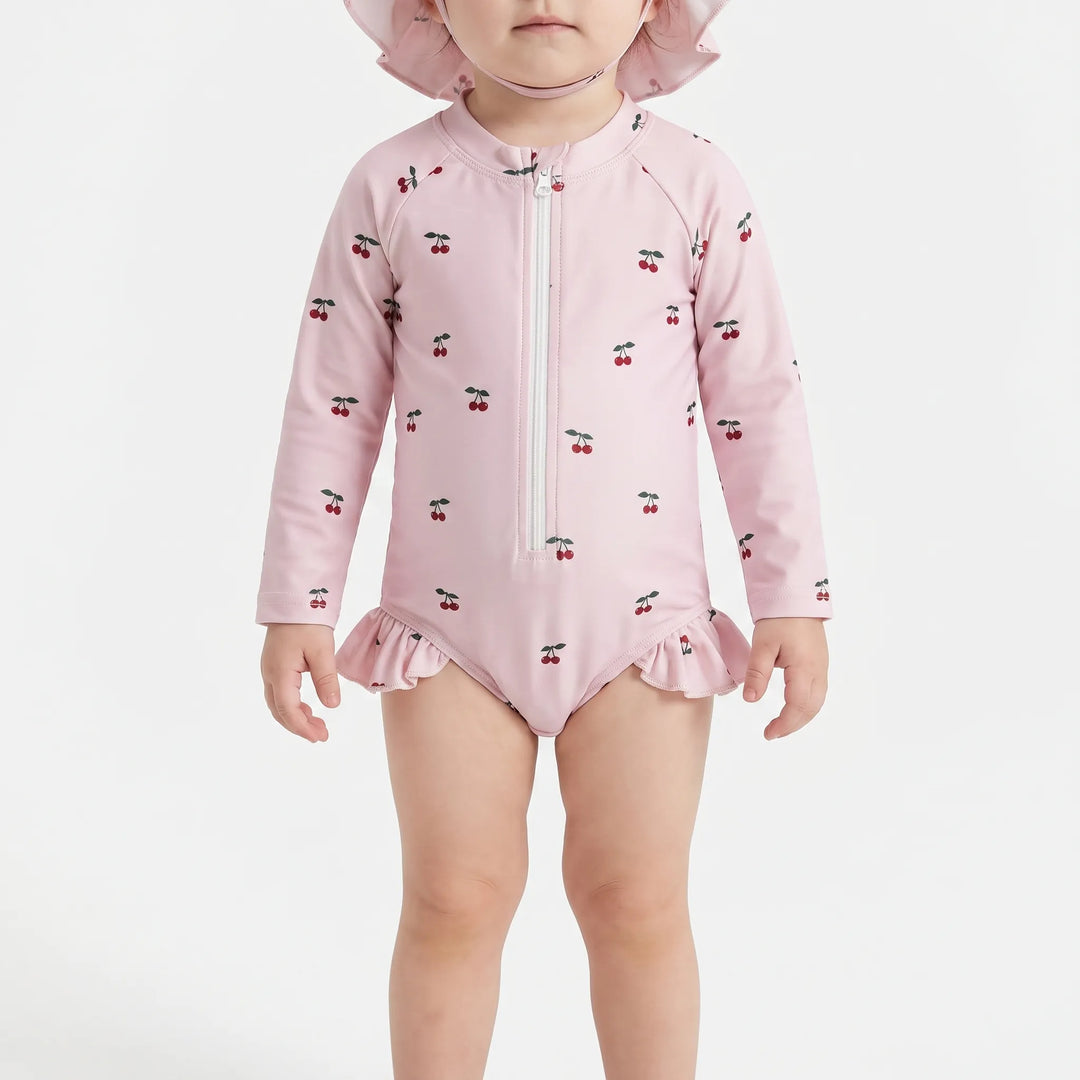 Close-up front view of a baby cherry-print long-sleeve swimsuit and matching hat on a white background