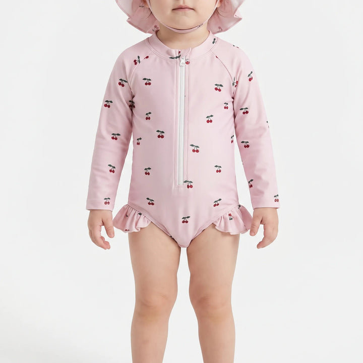 Close-up front view of a baby cherry-print long-sleeve swimsuit and matching hat on a white background