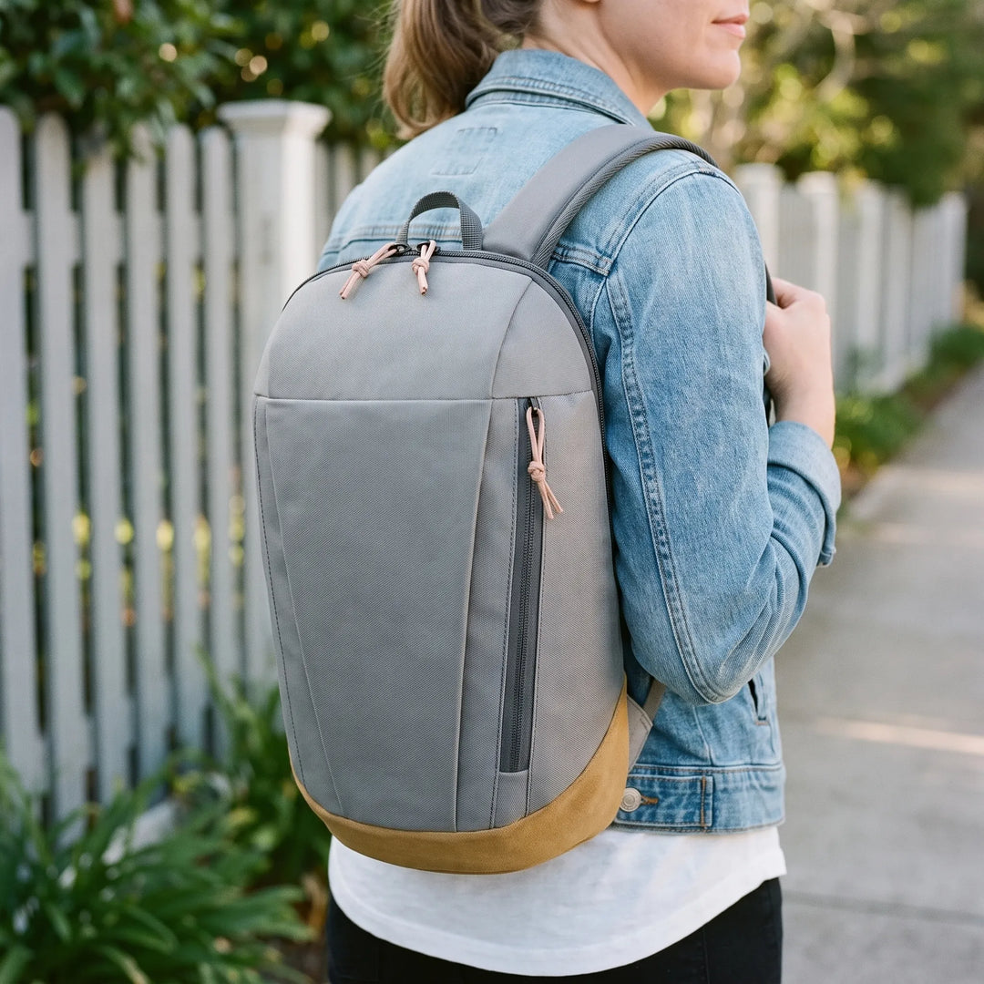 Woman wearing grey lightweight mini hiking rucksack outdoors near a white fence