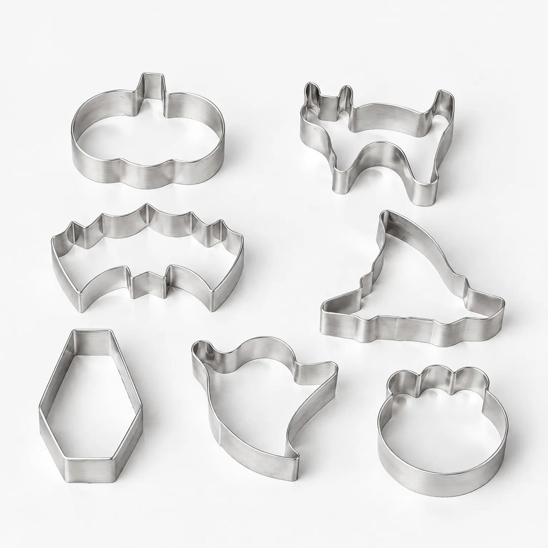 Assorted spooky baking tools and metal cookie cutters laid out for festive Halloween pastries.