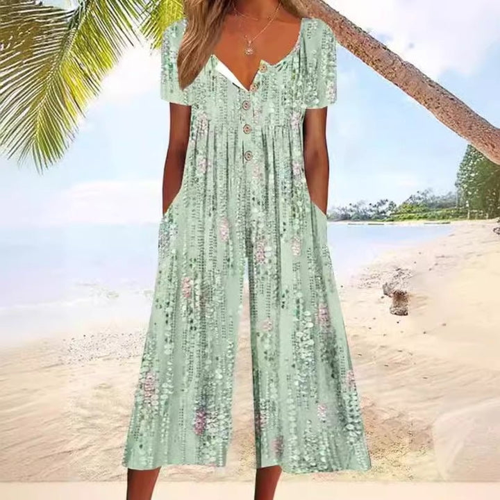Woman wearing green patterned V-neck short sleeve wide-leg jumpsuit by a sunny sandy beach
