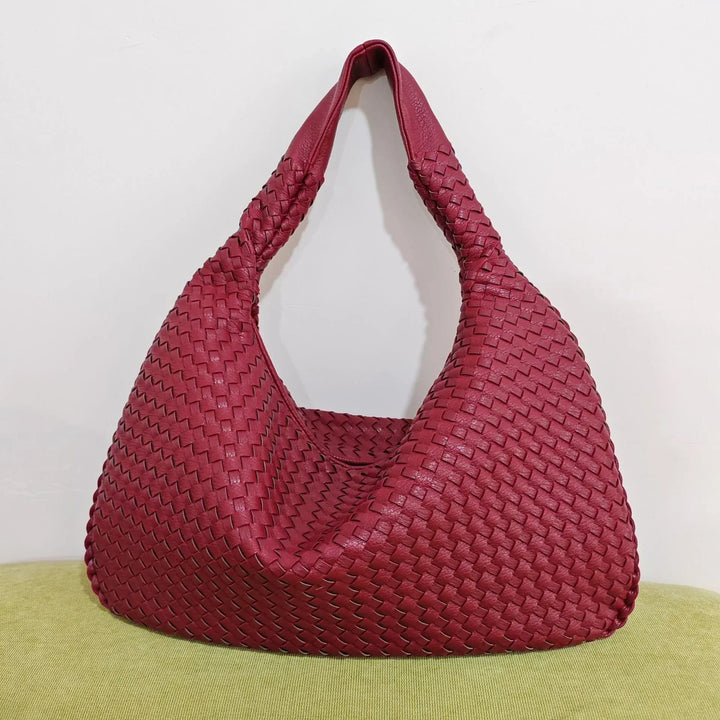 Wine red woven shoulder bag sitting on a green surface highlighting the rich color and design