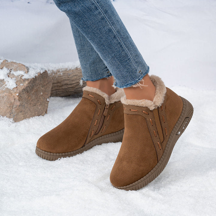 Close-up of brown women's winter ankle boots worn with jeans on snow.