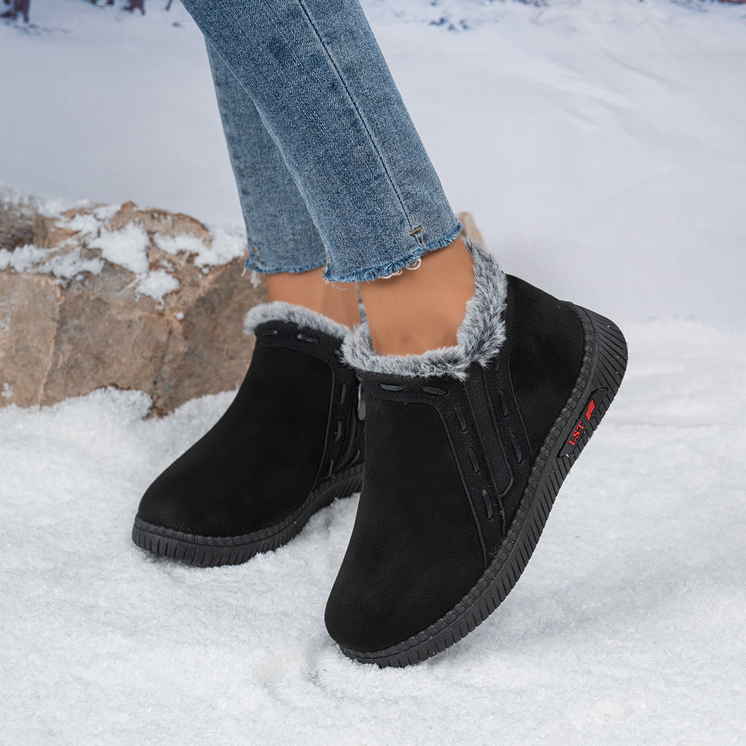 Close-up of black women's winter ankle boots with faux fur lining worn on snow.