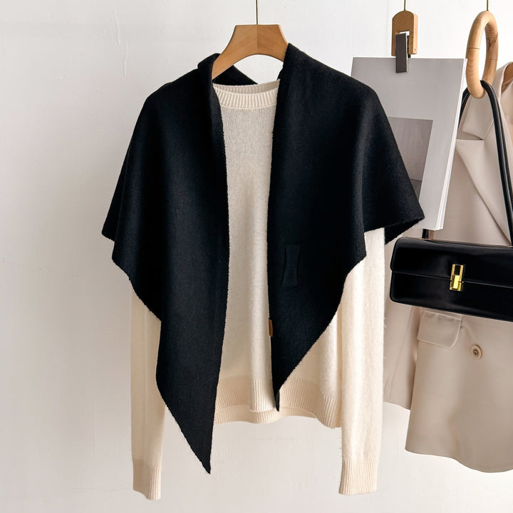 Black oversized knitted shawl hanging on a wooden hanger next to a cream sweater