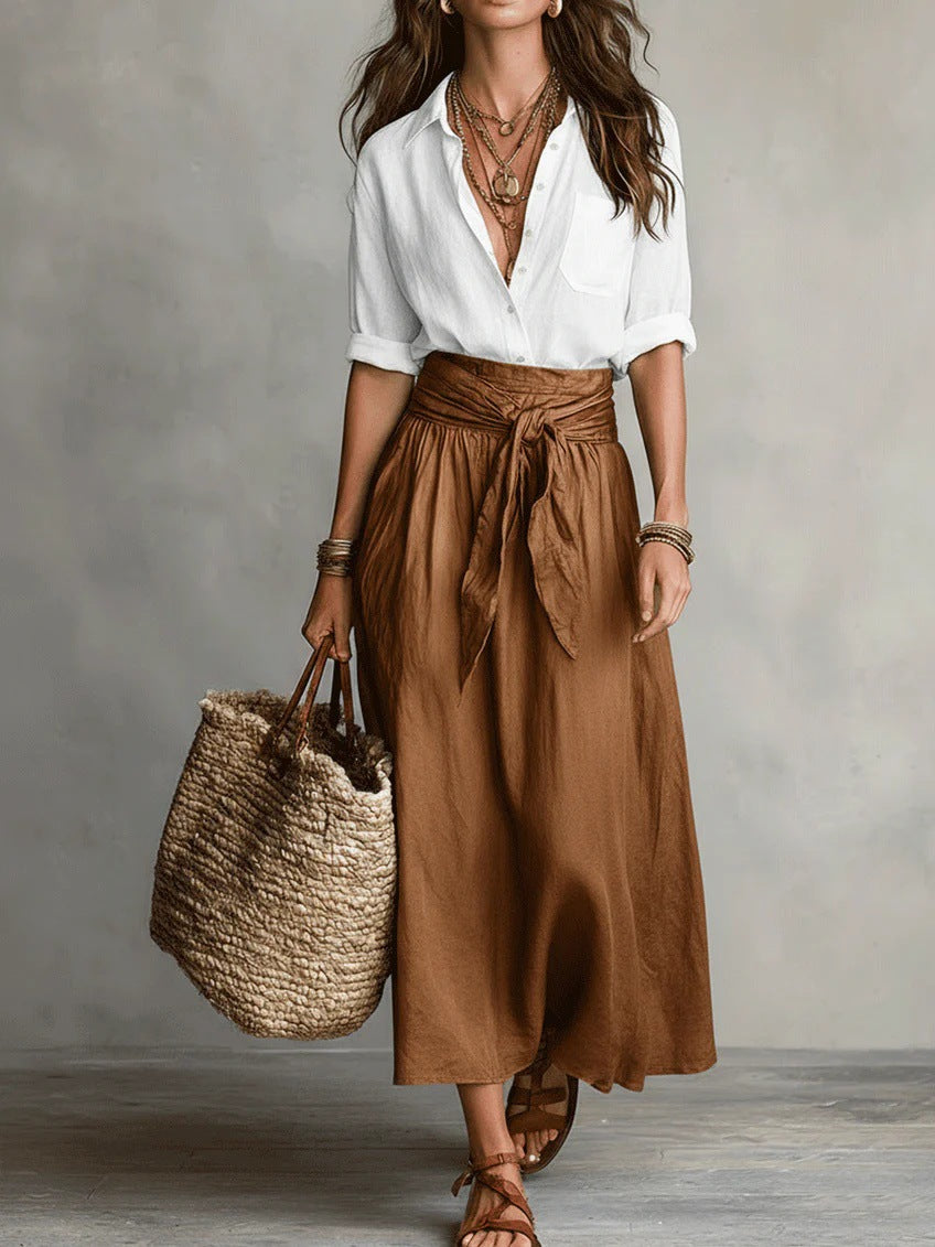 Woman wearing a white button-down shirt and brown tie-waist midi skirt with layered necklaces