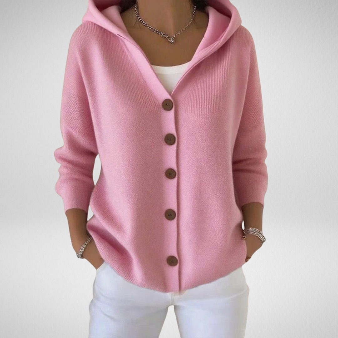 Woman wearing a pink hooded button knit cardigan with white pants and a silver chain necklace.