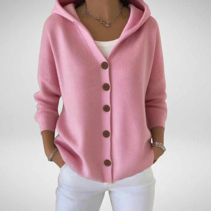Woman wearing a pink hooded button knit cardigan with white pants and a silver chain necklace.