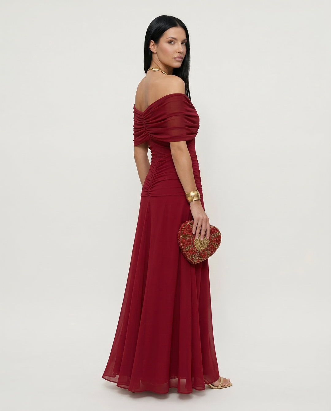Full-length side profile of a woman posing in a red off shoulder draped maxi dress