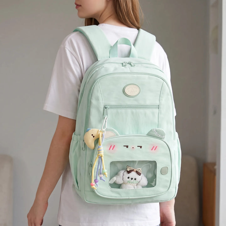 Back view of a person wearing a light green preppy daypack with a transparent front pocket displaying a plush toy