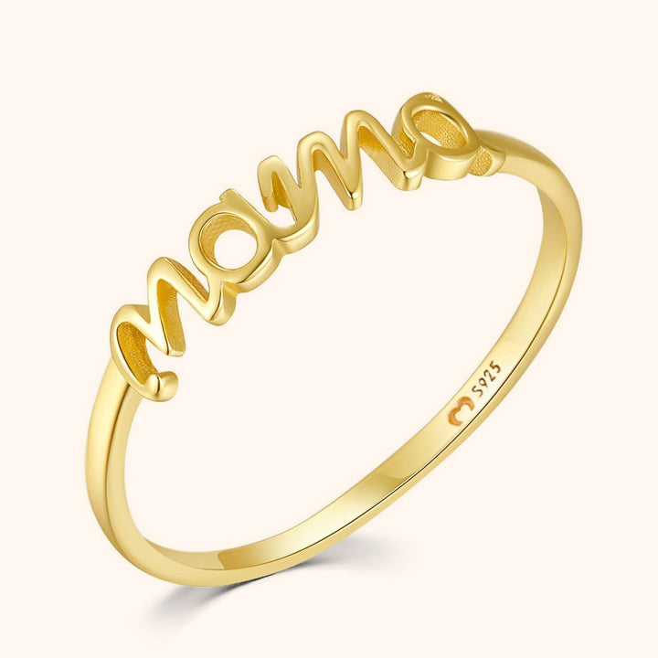 Close up of a gold Mama letter ring resting on a light background showing the polished metal finish.