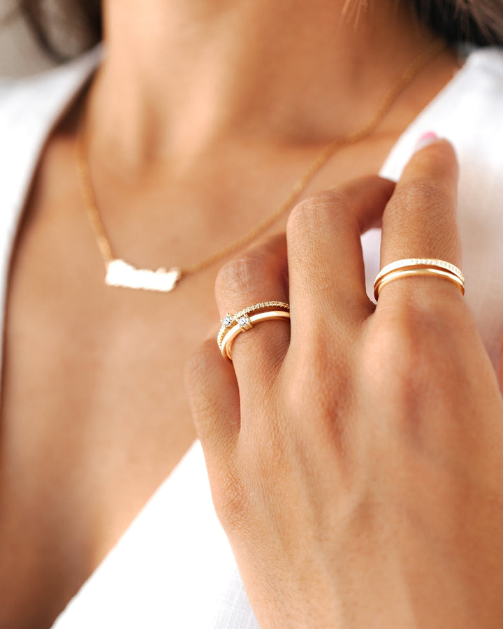 Woman wearing a gold double zirconia ring on her hand alongside a delicate necklace.