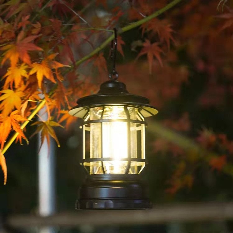 Retro camping lantern hanging from a tree branch glowing warmly outdoors