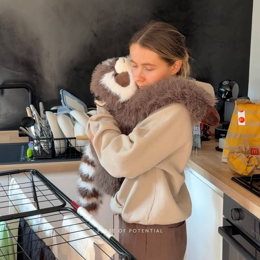 Woman hugging the weighted raccoon plush around her neck and shoulders in a kitchen