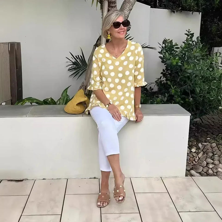 Woman wearing yellow polka dot V-neck tee sitting on a stone bench