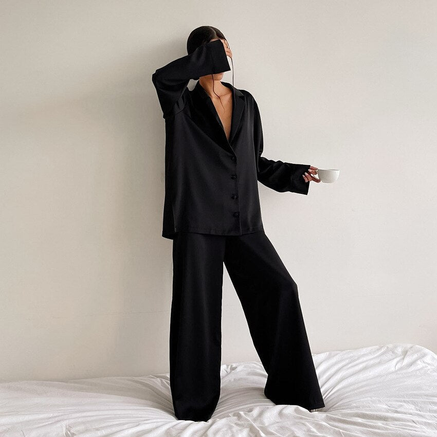 Model standing in a black satin pyjama set holding a coffee cup