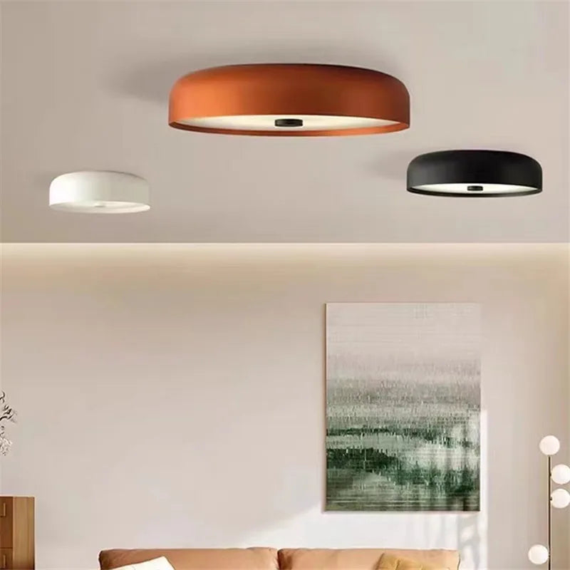 Three modern minimalist LED ceiling lights in rust, white, and black mounted on a ceiling.