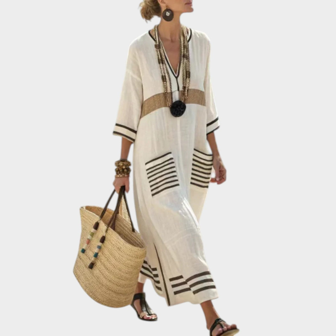 Woman walking in a white maxi dress with beige striped detailing and layered necklaces