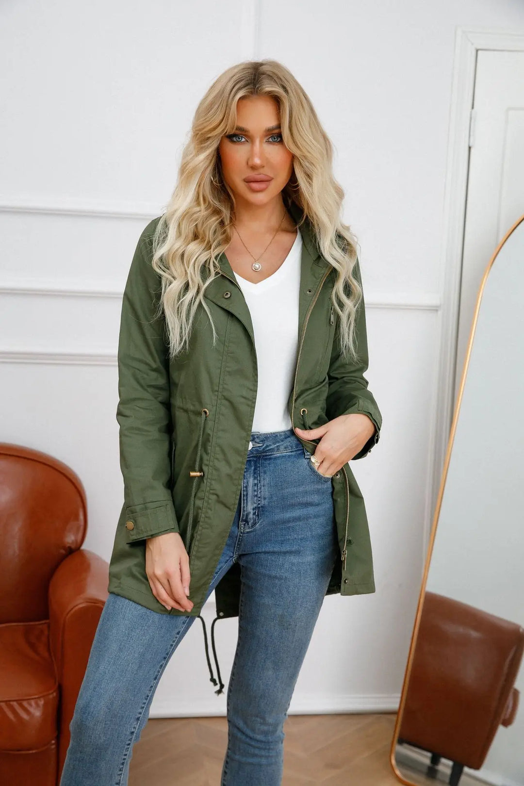 Woman wearing green hooded jacket with adjustable waist standing indoors