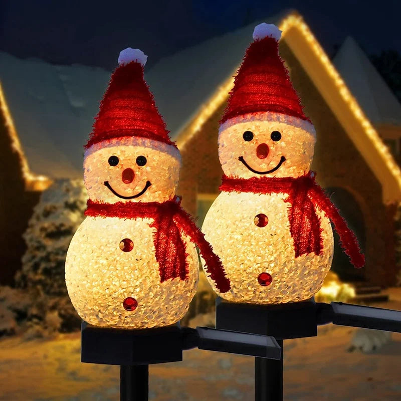 Two illuminated snowman solar garden stakes lighting up an outdoor pathway at night
