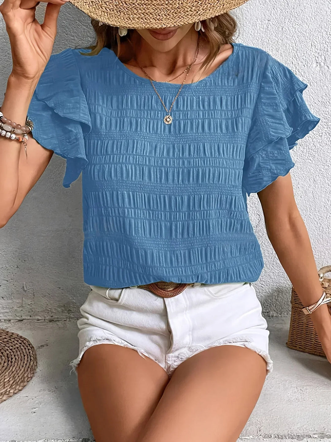 Woman wearing a malachite blue short ruffle sleeve blouse paired with white denim shorts