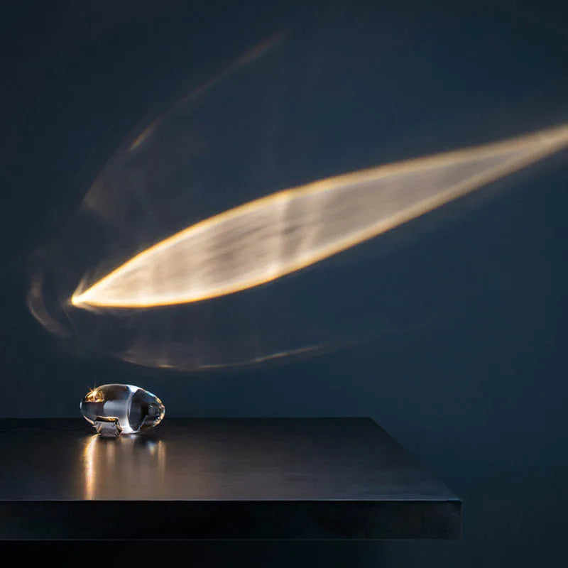 Sleek crystal projection lamp resting on a dark surface with atmospheric beam