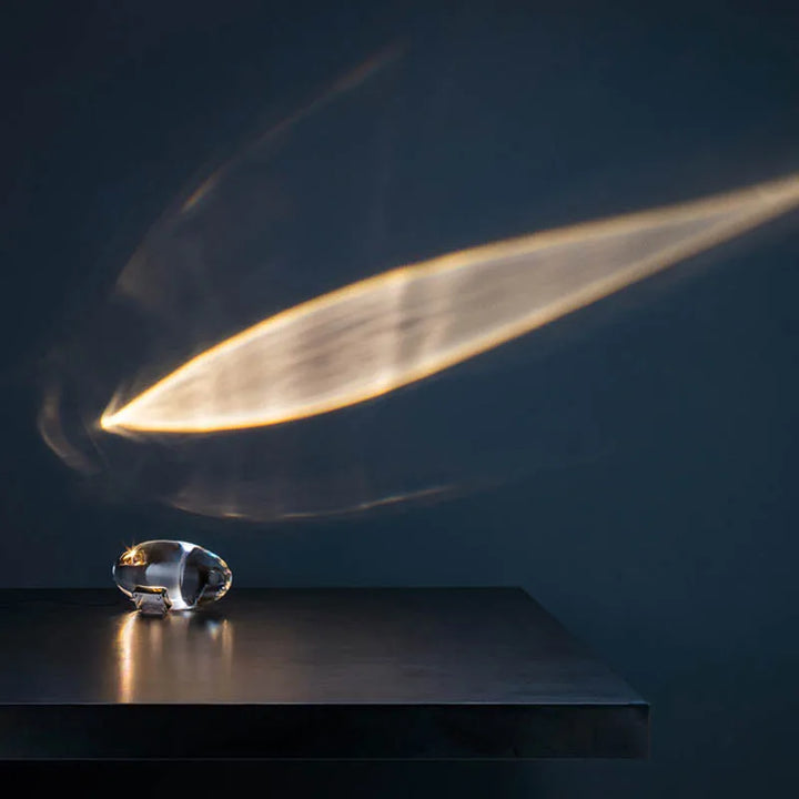 Sleek crystal projection lamp resting on a dark surface with atmospheric beam