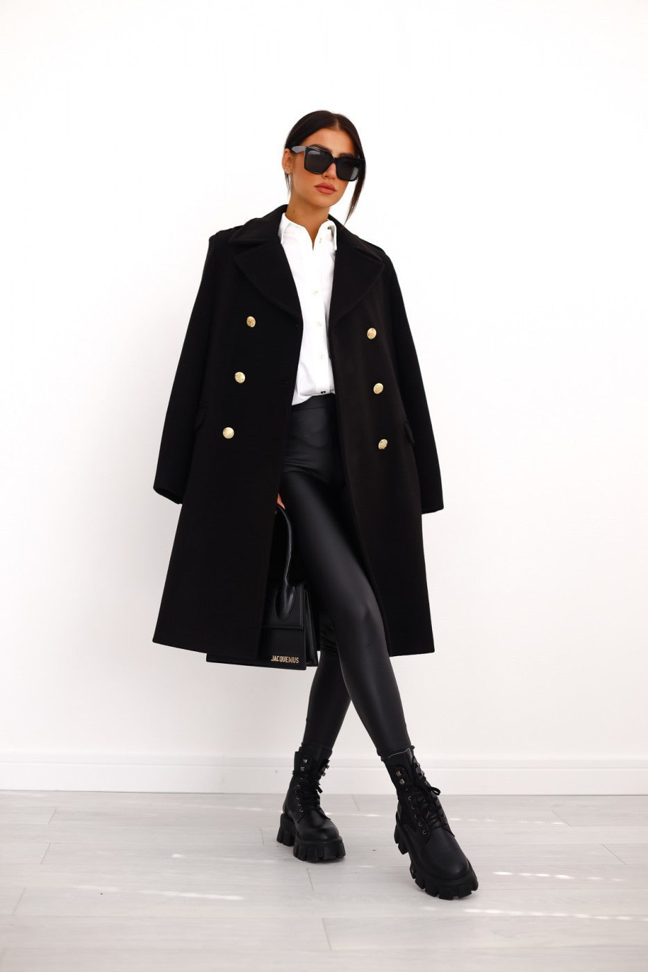 Model wearing a black double-breasted long trench coat from the front