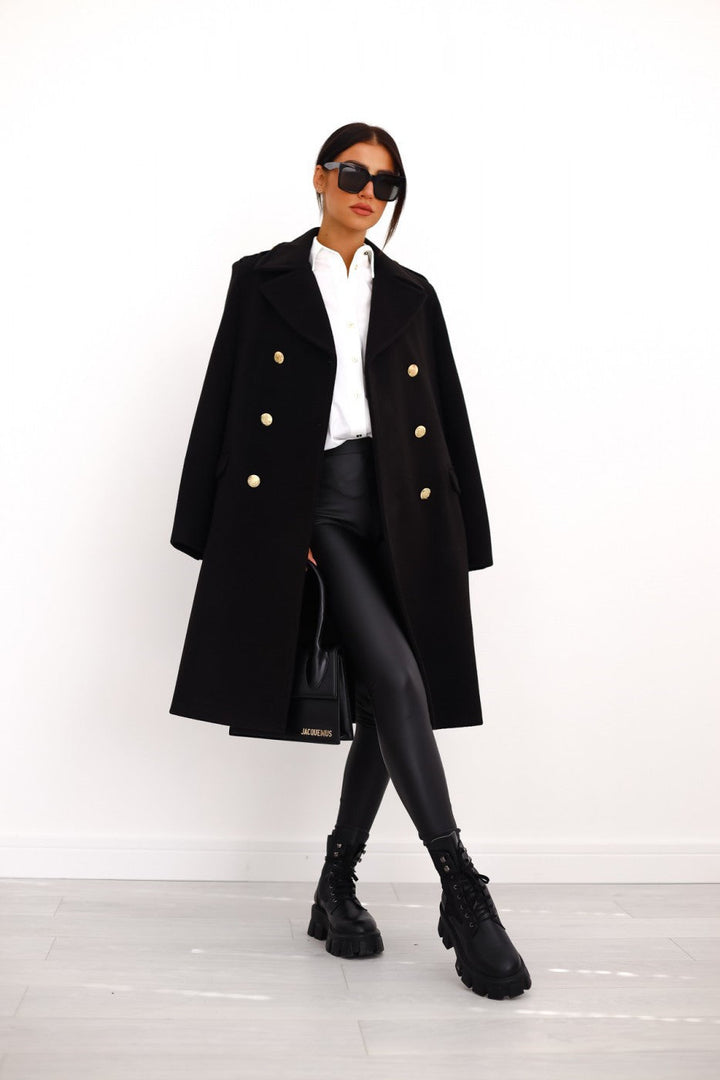 Model wearing a black double-breasted long trench coat from the front