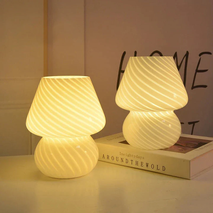 Two vintage striped glass mushroom table lamps casting a warm glow on a white surface